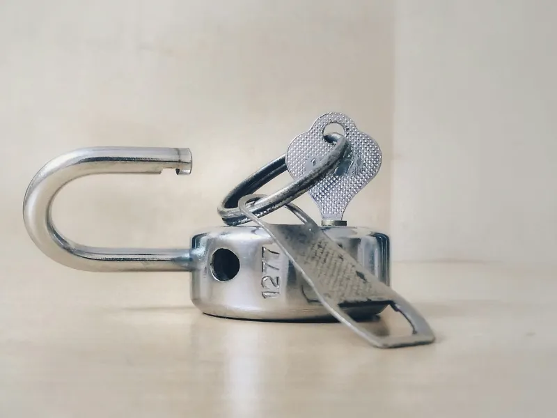 Close-up of a shiny silver metal padlock unlocked with keys placed inside its shackle on a neutral surface.