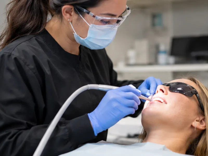 Dentist wearing protective gear treating patient using dental tools in a modern clinic setting.
