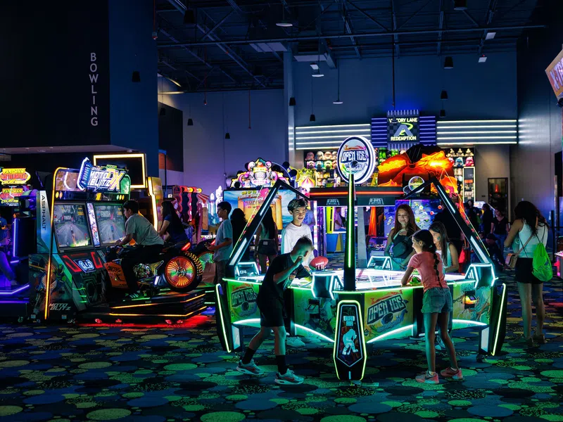 Children and teens playing various brightly lit arcade games in an indoor entertainment center at night.