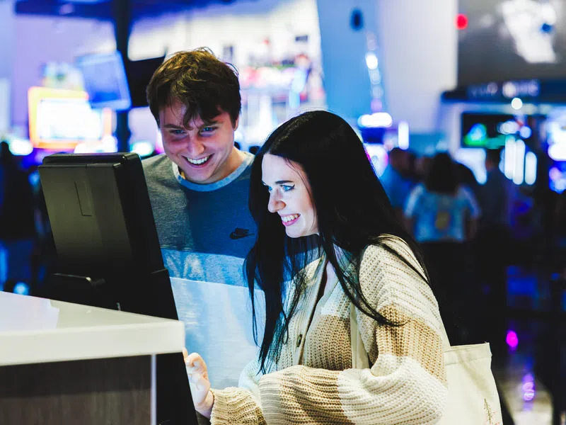 Young man and woman enjoying interactive touchscreen games in a vibrant arcade setting with colorful lights.
