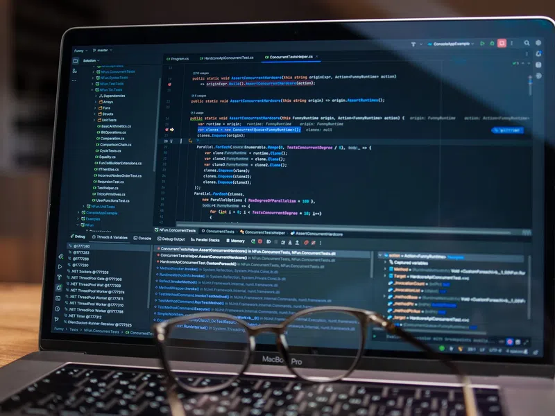 Open laptop displaying a software development environment with code and debugging tools, with glasses in front.