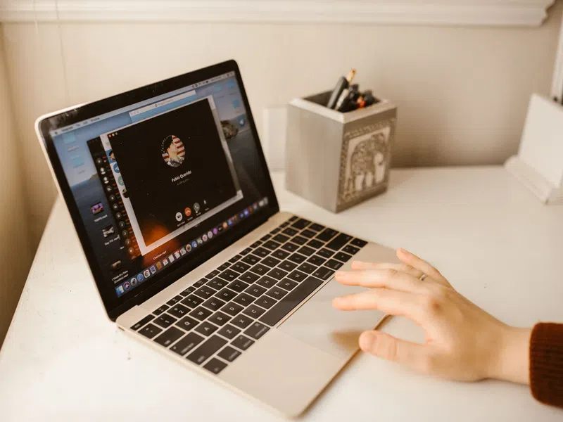 Person's hand using a MacBook with a video call screen open on a clean white desk near a pencil holder.