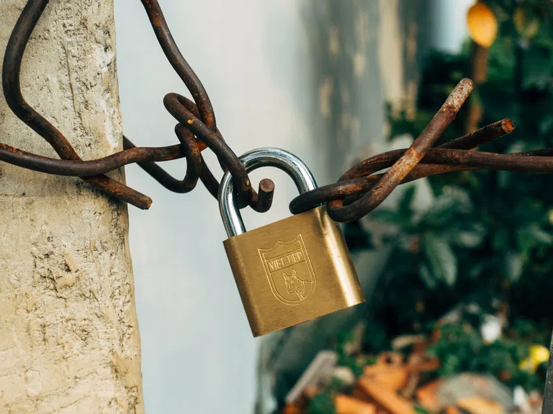 Rusty twisted metal wires secured with a brass padlock attached to a concrete post outdoors.