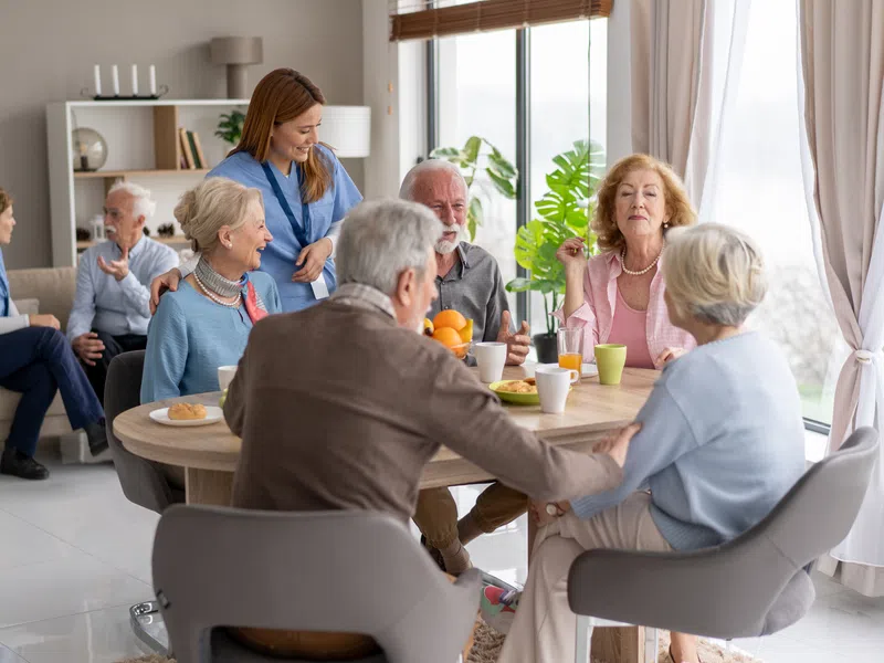 Caregiver and a group of seniors gathered together at a table