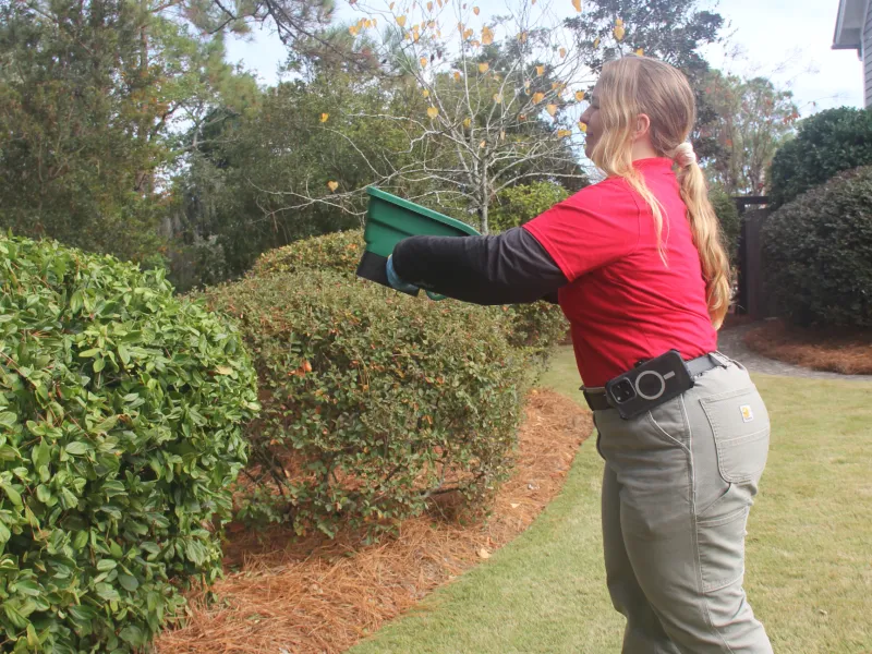 a woman holding a green bin applying pest control