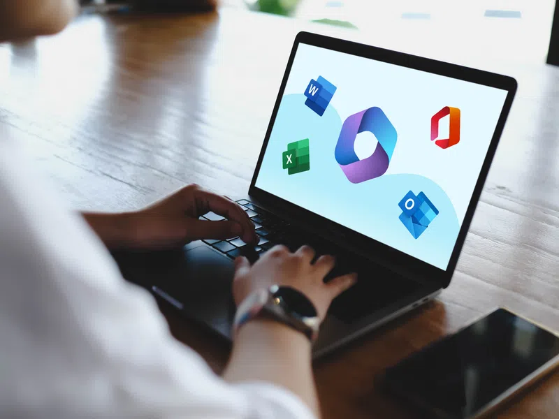 Person using laptop displaying Microsoft Office app icons on screen including Word, Excel, Outlook, and Office 365.