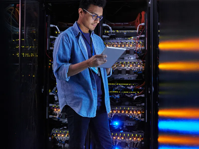 Technician using a tablet to check and maintain servers in a data center with colorful LED lights.