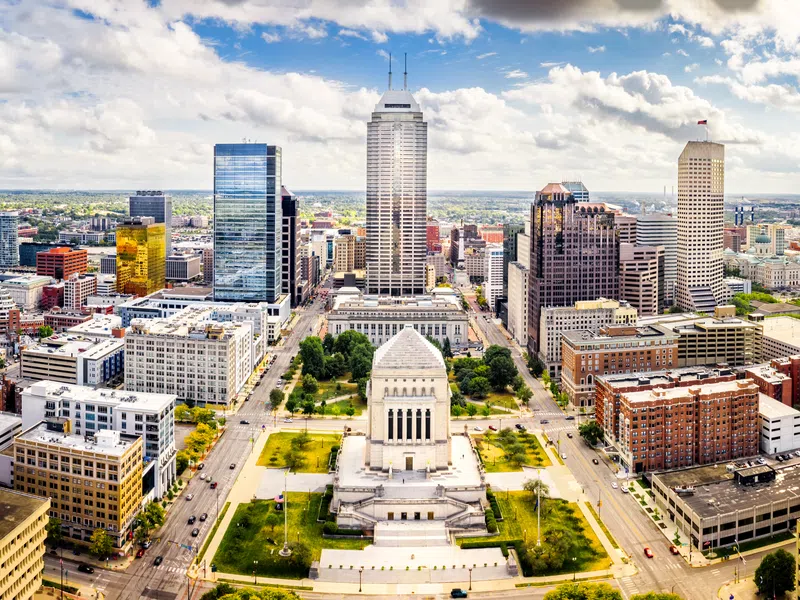 Aerial view of Indianapolis skyline with Soldiers and Sailors Monument at center under cloudy blue sky.