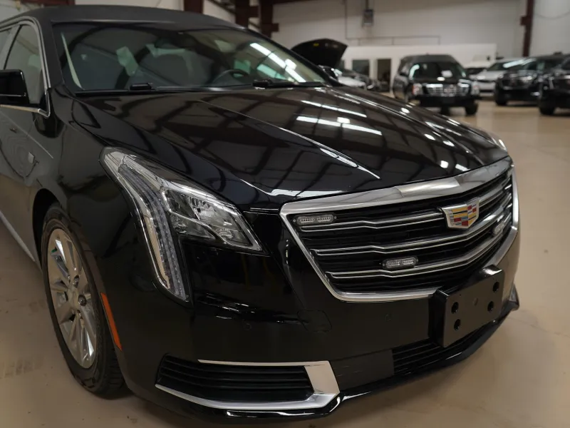 Black Cadillac sedan parked inside a well-lit car showroom with multiple vehicles in the background