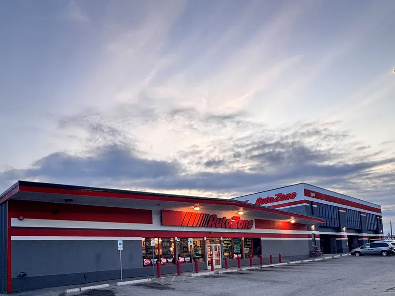 AutoZone store exterior at dusk with red and gray facade and illuminated signage under a cloudy sky.