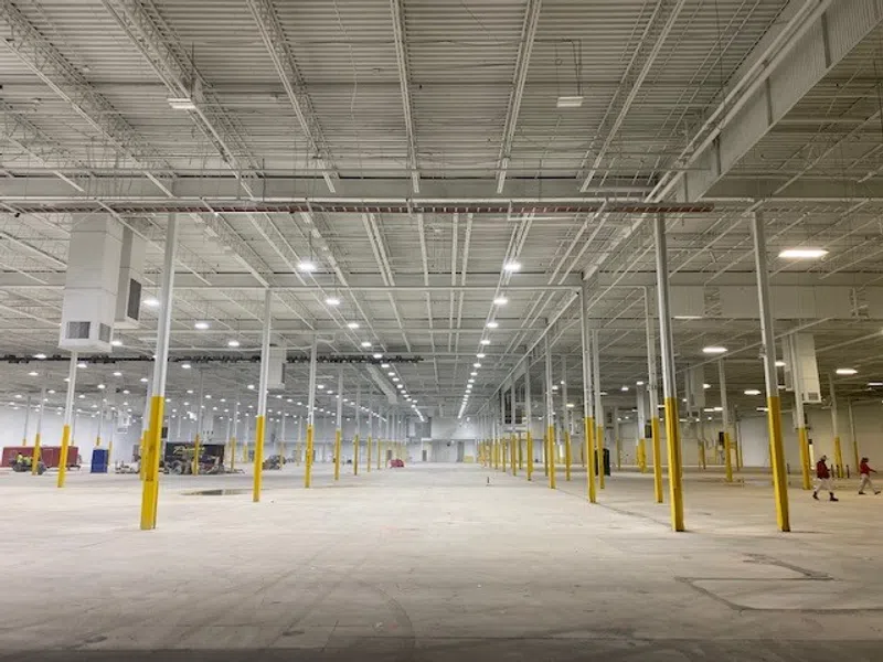 Spacious empty warehouse interior with high ceiling, yellow safety poles, and bright overhead lighting