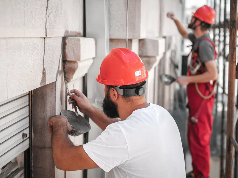 Construction workers in safety helmets restoring stone masonry on a building facade scaffold.