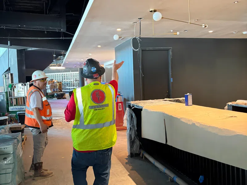 Two construction workers in safety vests and helmets discuss progress inside a building under renovation.