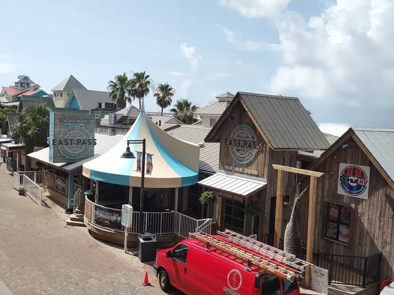 Street view of rustic shops including East Pass Seafood and a red service van parked outside on a sunny day.