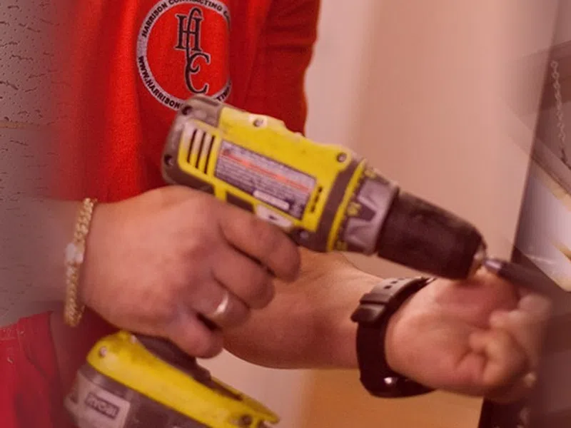 Worker in red shirt using a yellow cordless drill for a home improvement task indoors.