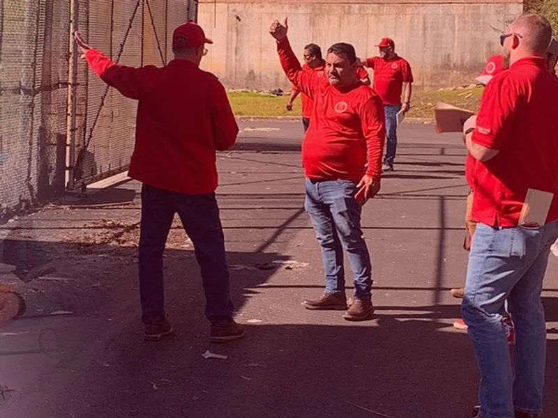 Team meeting indoors with members in red shirts at table and outdoor discussion in sunny open area