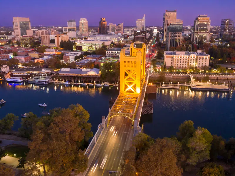 Aerial view of illuminated Tower Bridge over Sacramento River with city skyline at dusk.