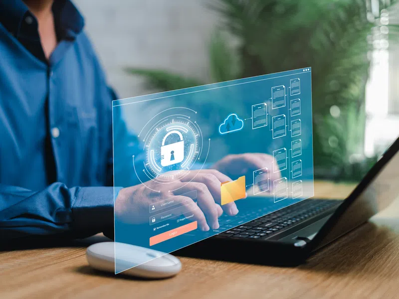 Person typing on laptop with digital security interface showing locked padlock and cloud data icons.