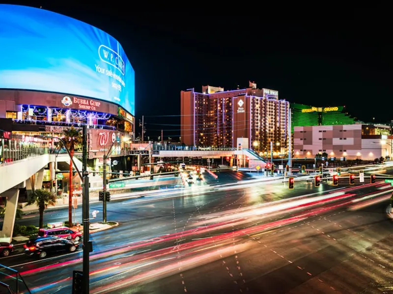 Busy Las Vegas city intersection at night with light trails and illuminated hotels and billboards.