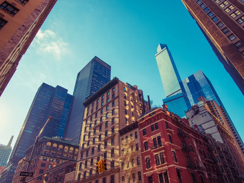 Sunlit urban cityscape with a mix of historic and modern skyscrapers under a clear blue sky.