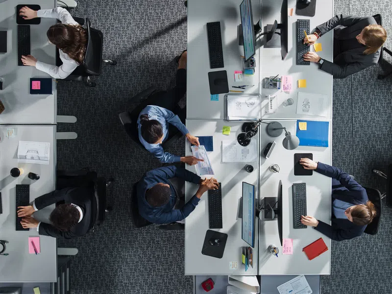 Top-down view of a busy modern office with employees working at desks and collaborating in teams.