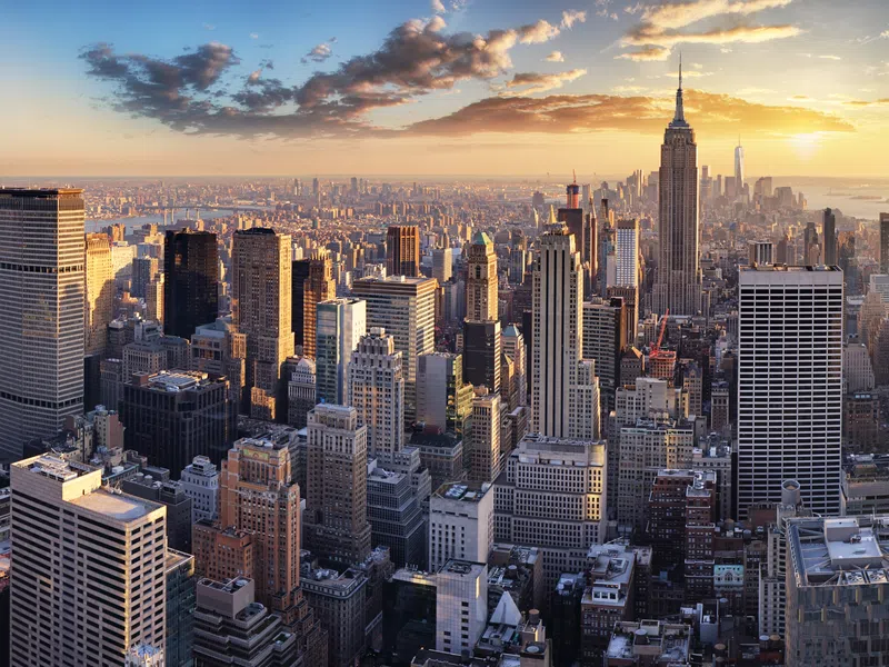 New York City skyline with Empire State Building at sunset, skyscrapers, and partly cloudy sky.