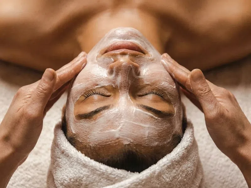 Close-up of a woman receiving a relaxing facial massage with skincare cream and a towel wrap.