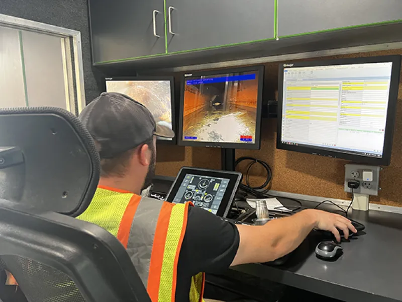 Operator monitors multiple screens in a control room, managing tasks with a tablet and desktop setup.