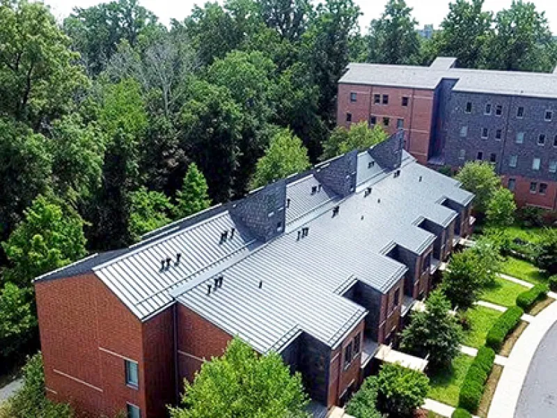 Aerial view of metal roof installation on Lakeside Graduate Apartments student housing complex surrounded by trees