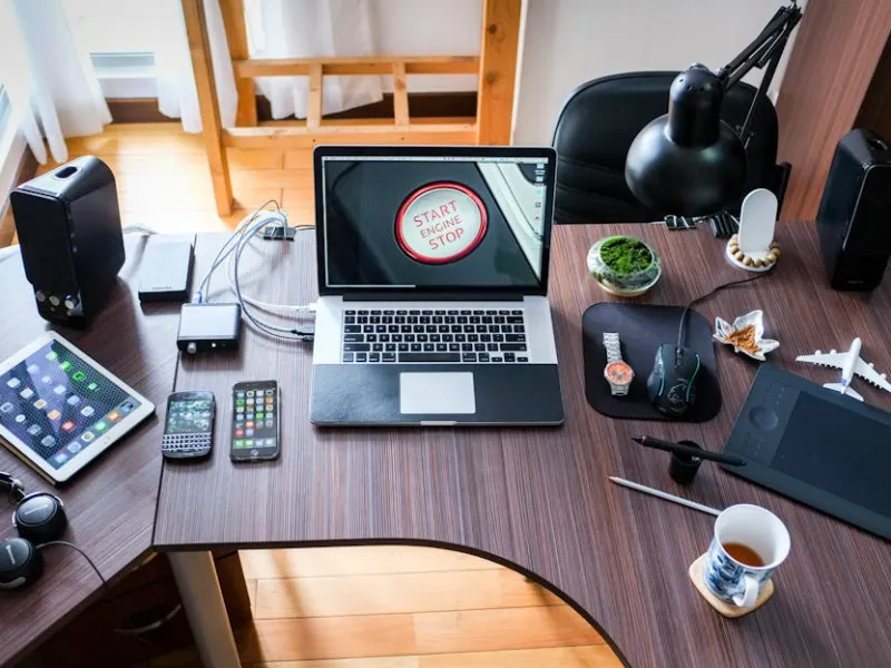 Modern workspace with laptop, tablets, smartphones, headphones, desk lamp, and coffee on a wooden desk