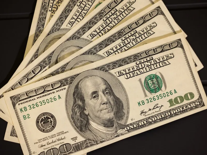 Close-up of multiple one hundred dollar US bills fanned out on a dark surface