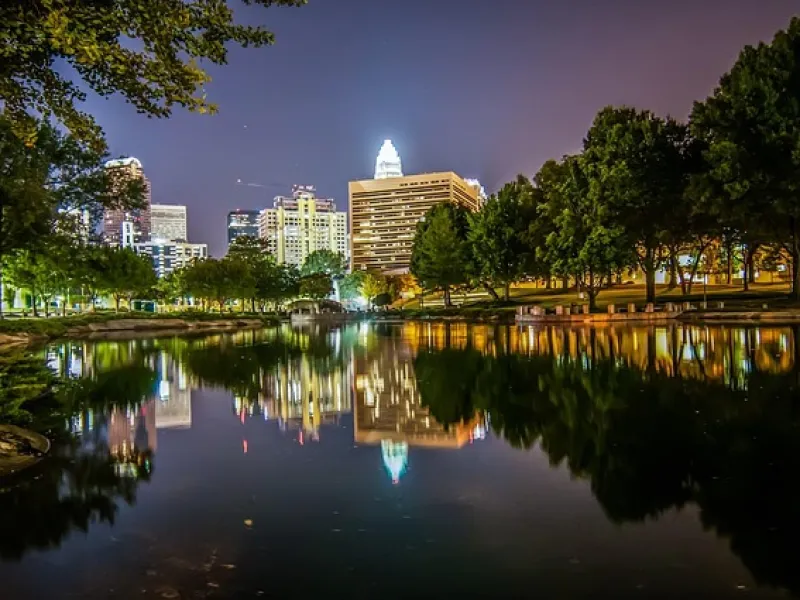 City skyline reflected in a calm river at night with illuminated buildings and surrounding trees
