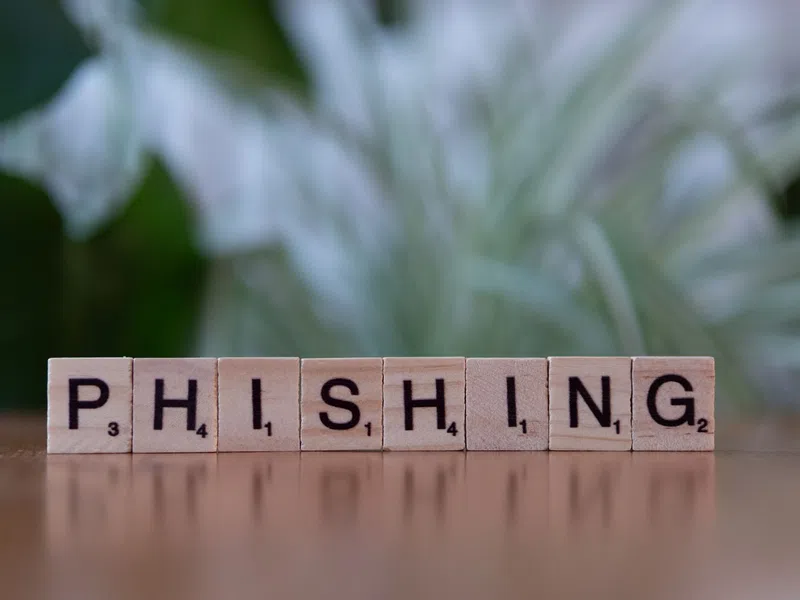 Scrabble tiles spelling phishing on a reflective surface with blurred green and white background.