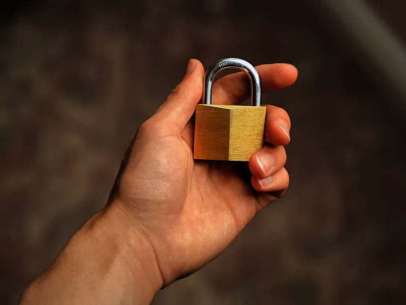 Close-up of a hand holding a small brass padlock with a blurred background for security concept.