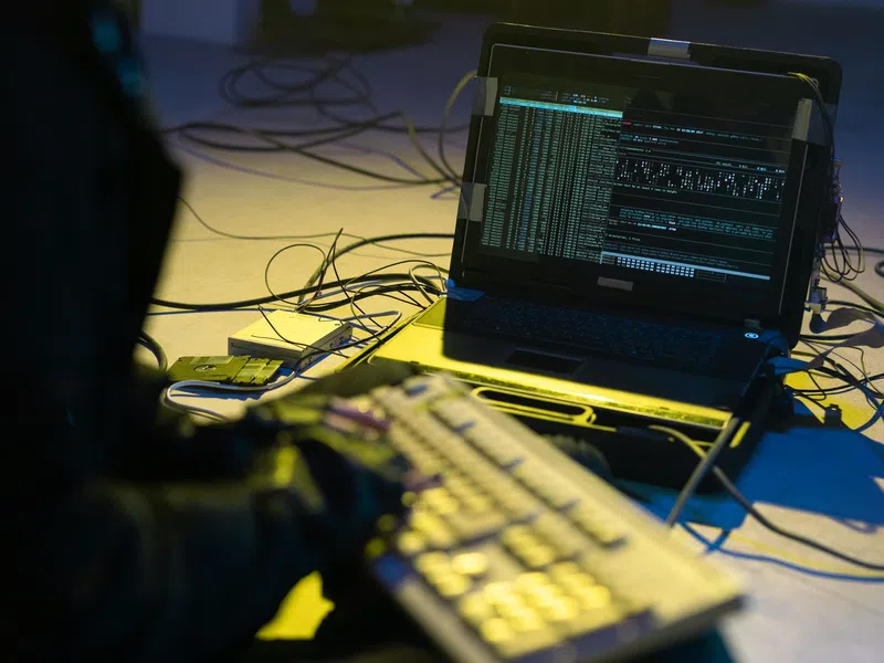 Person typing on keyboard connected to laptop displaying complex code and data with multiple cables around.