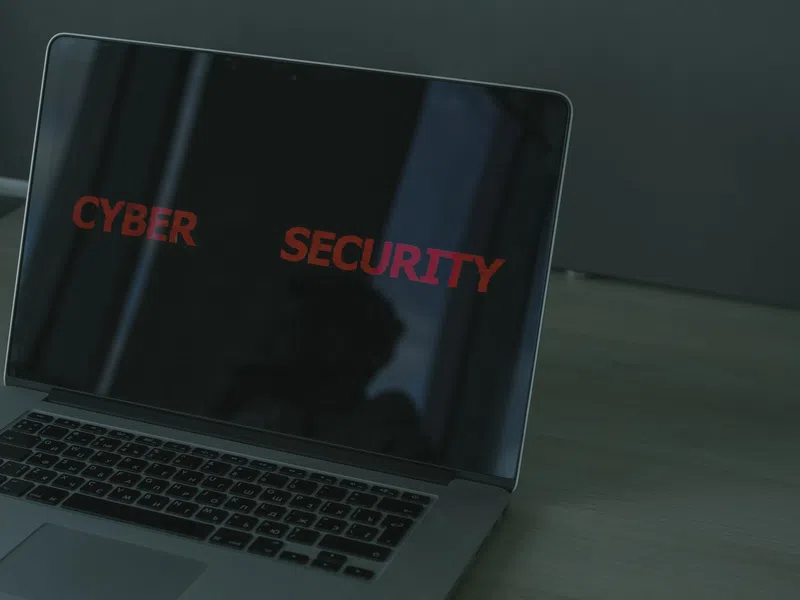 Laptop screen displaying red text 'CYBER SECURITY' on a dark background on a wooden desk.