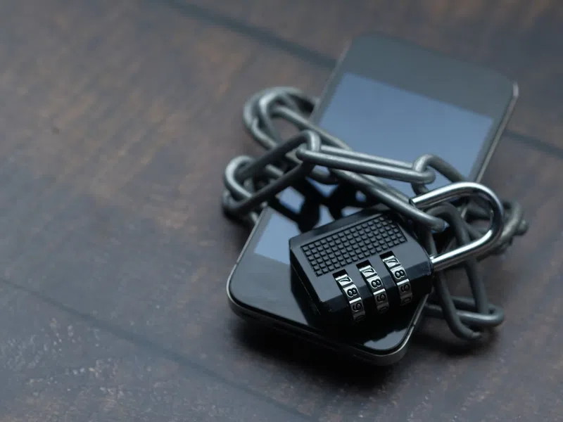 Smartphone wrapped in metal chains secured with a combination padlock symbolizing phone security and data protection.