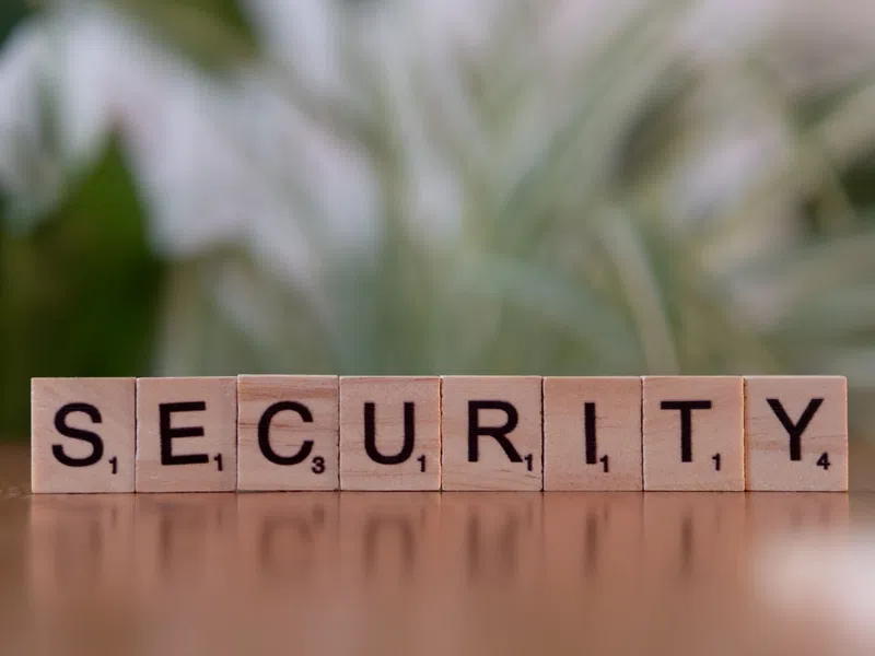 Wooden Scrabble tiles spell out the word SECURITY on a reflective surface with blurred greenery background.