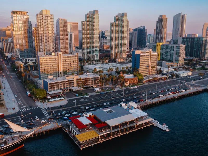Aerial view of a waterfront city pier with restaurants and high-rise buildings at sunset.