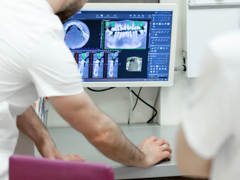 Dentist analyzing dental X-ray images on computer screen during patient consultation in clinic.