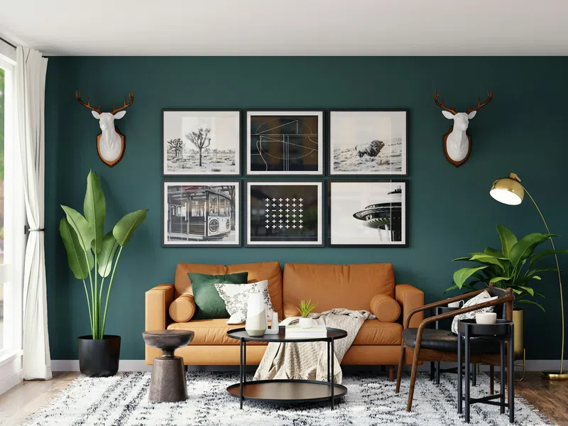 Modern living room with green accent wall, brown sofa, framed art, plants, and natural light from large windows