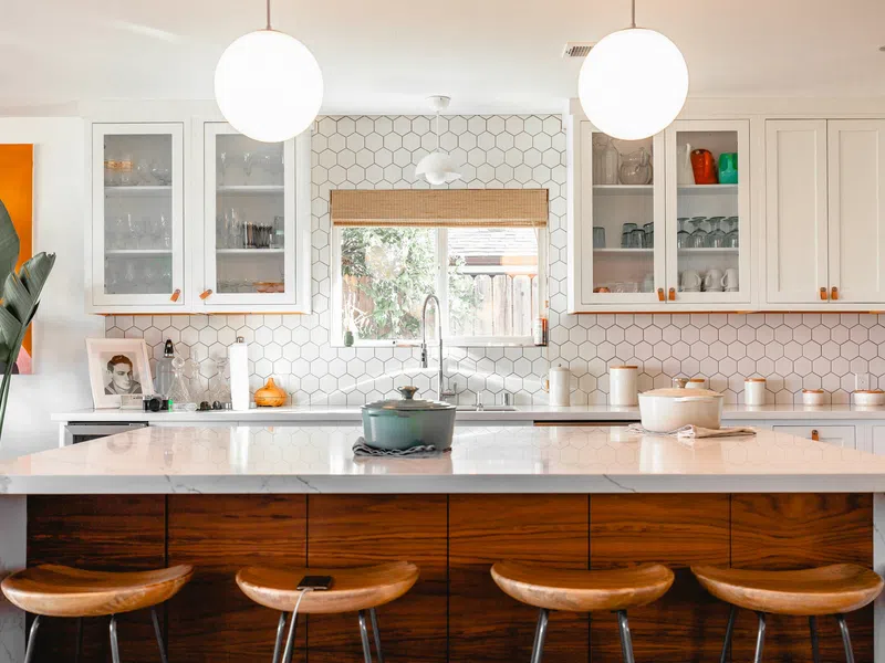 Bright modern kitchen with white hexagonal tile backsplash, wooden island with stools, and pendant lights
