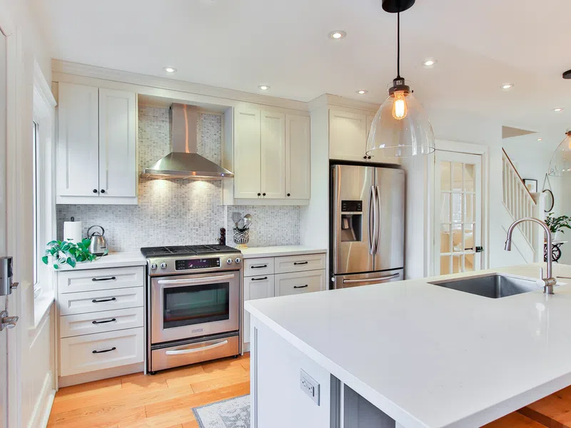 Modern white kitchen with stainless steel appliances, large island, hardwood floors, and pendant lights