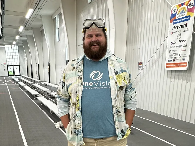 Man wearing snorkeling gear, shorts, and a patterned shirt inside an indoor track facility.