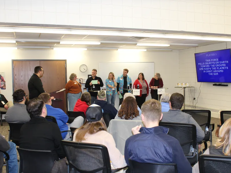 Group of people playing Jeopardy quiz game with question on screen about gravity and planets.