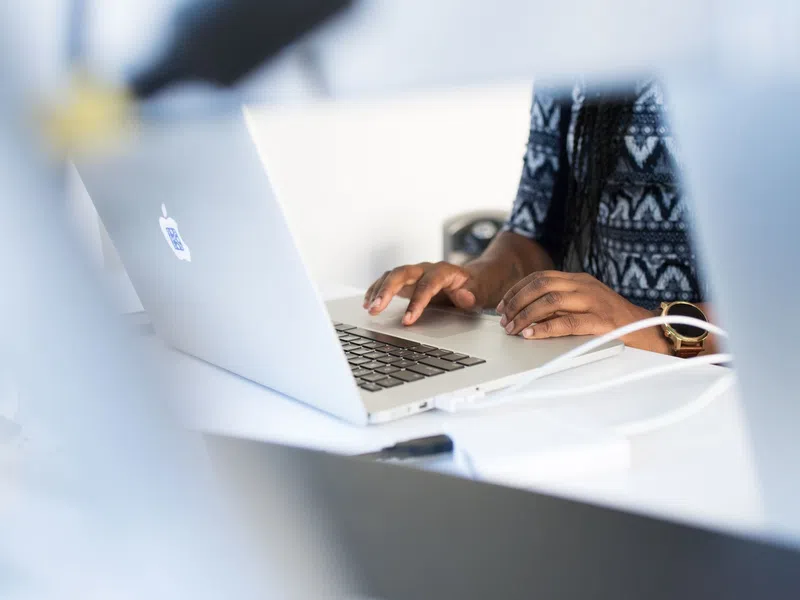 Person typing on a silver MacBook laptop at a white desk with charging cables connected.