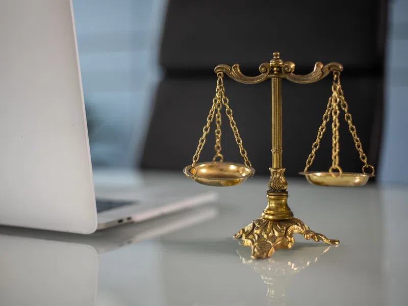 Golden balance scale on glass desk next to open laptop in modern office setting with blurred background.