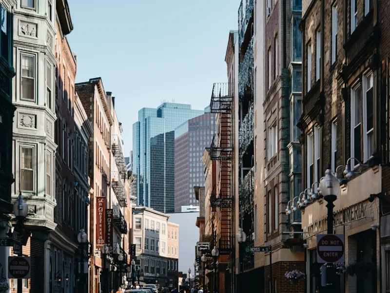 Historic city street lined with old brick buildings and modern skyscrapers in the background under a clear sky.