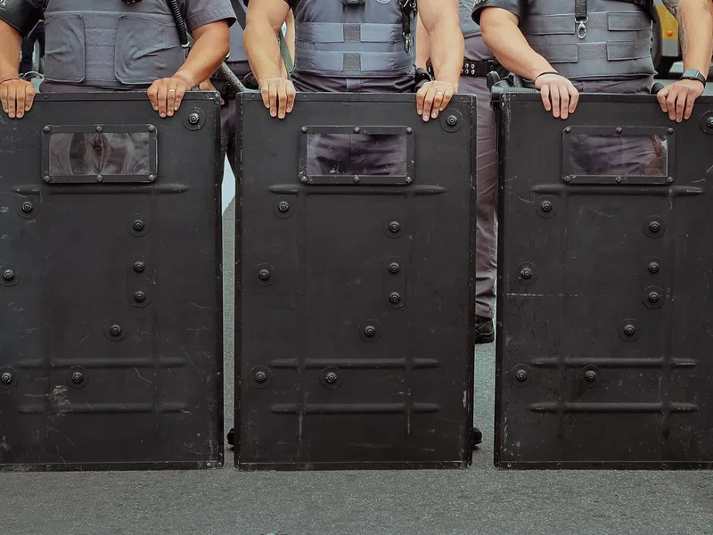 Police officers holding black riot shields in a line during a public safety operation.