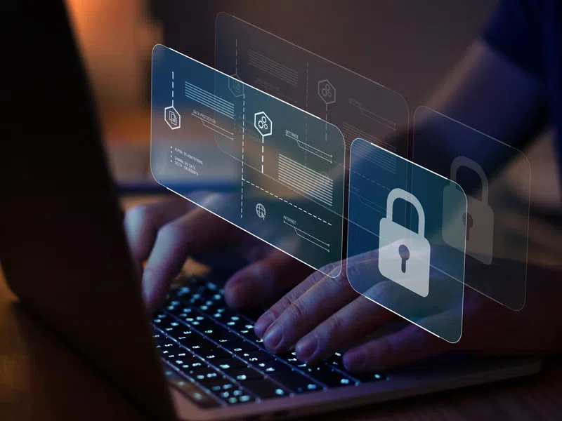 Person typing on laptop with digital security interface and lock icons representing online data protection.
